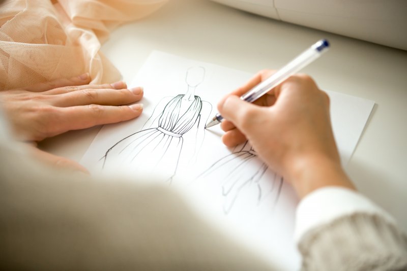 Hands drawing a clothing design sketch Hands drawing a black ink clothing design sketch, view over the shoulder, closeup, close-up